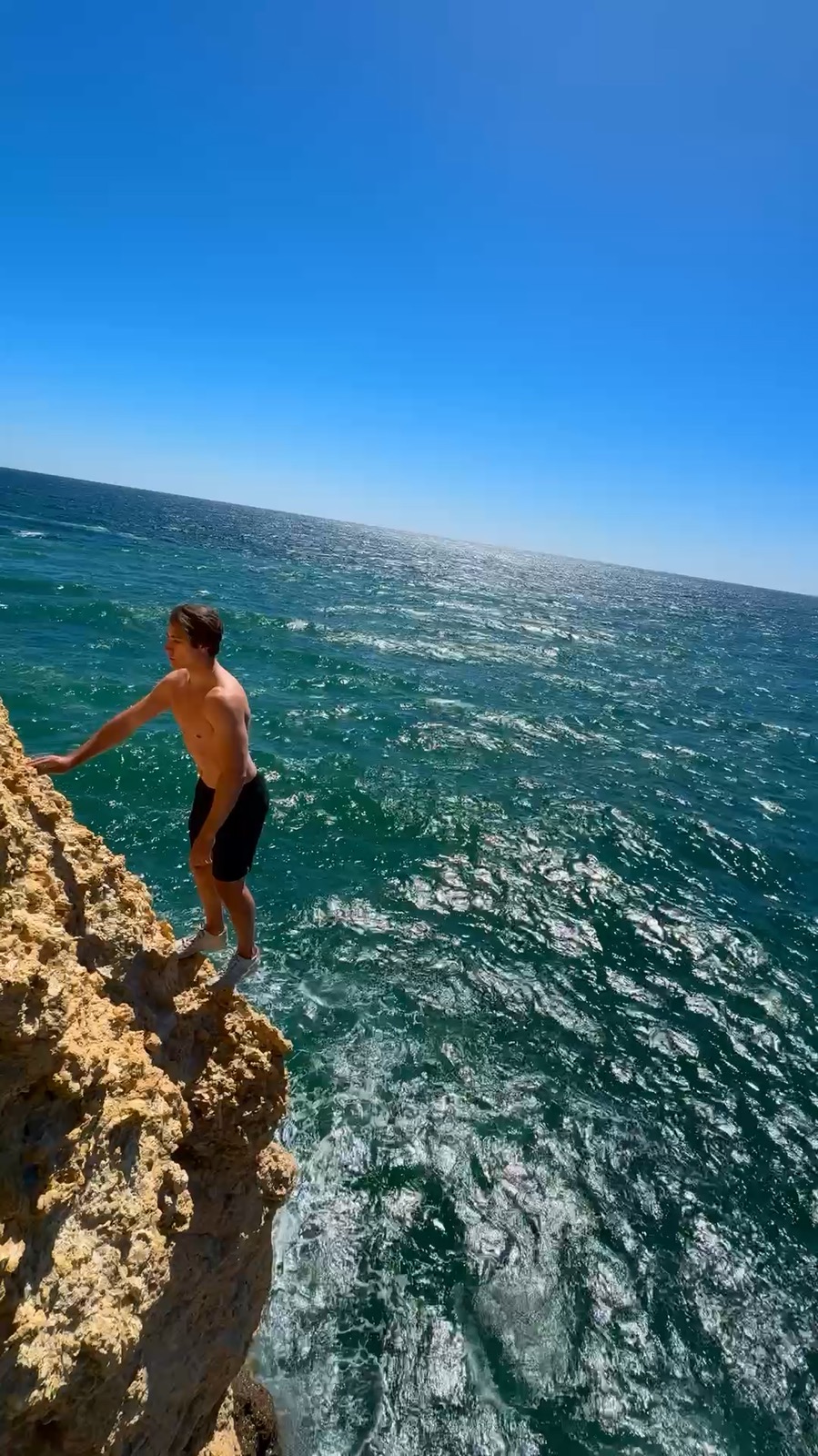 Angelo balancing on the edge of a sea cliff above the water