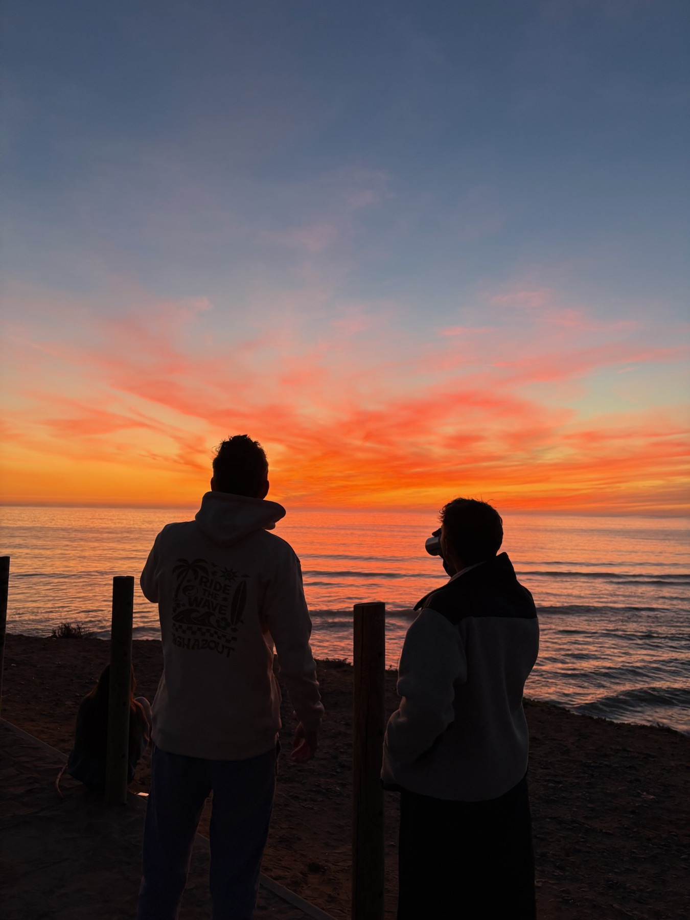 Two people watching a red sunset over the sea